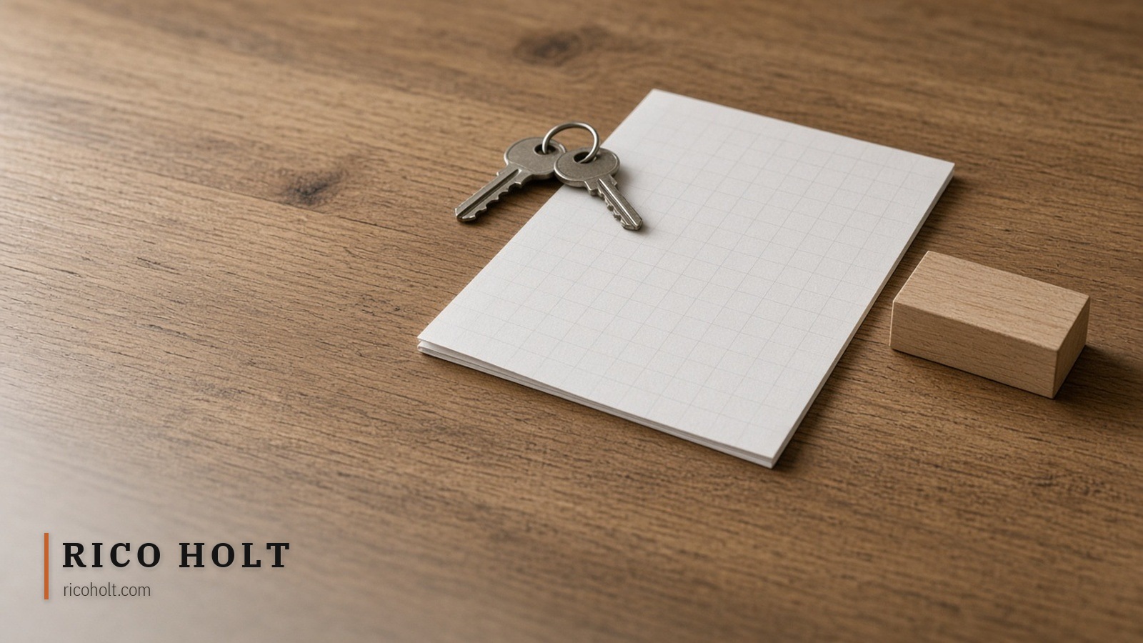 Metal keys on blank grid paper beside a plain wooden block on pale oak