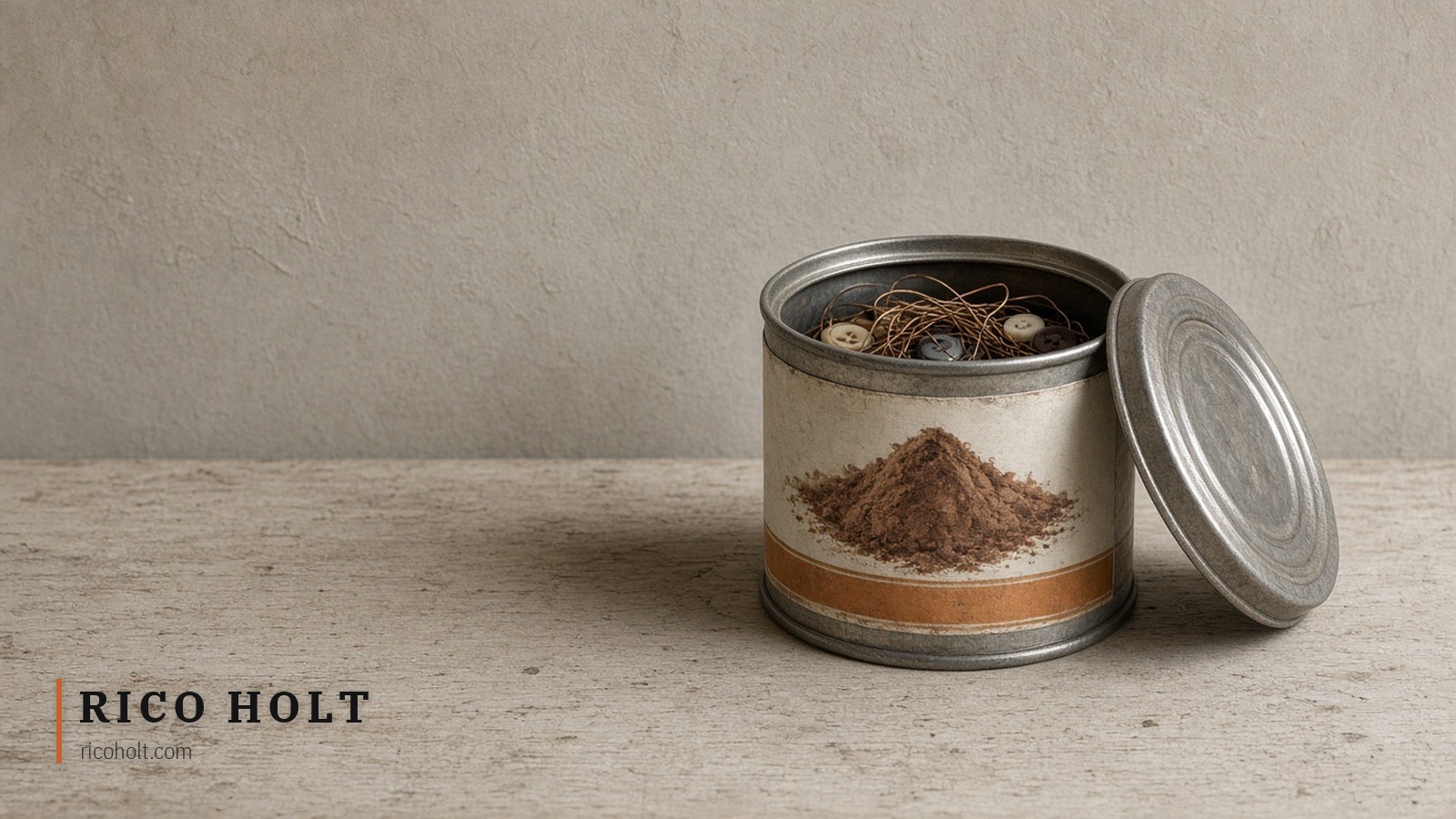 An open metal tin on a pale bench, its label painted with brown powder and an ochre band, holding copper wire and shirt buttons, its lid leaning beside it