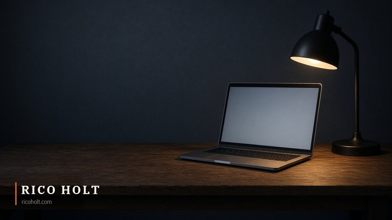 A laptop open on a dark wooden desk under a single desk lamp, in an empty dark room