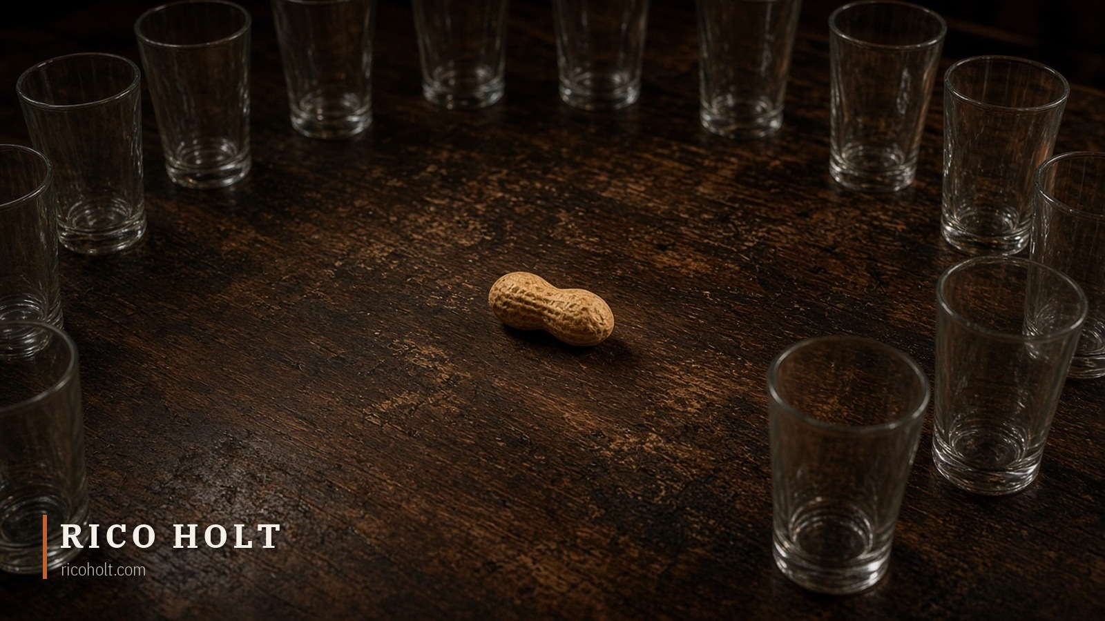 A single peanut in its shell at the centre of a dark wooden table, ringed by empty clear glasses, with the Rico Holt wordmark